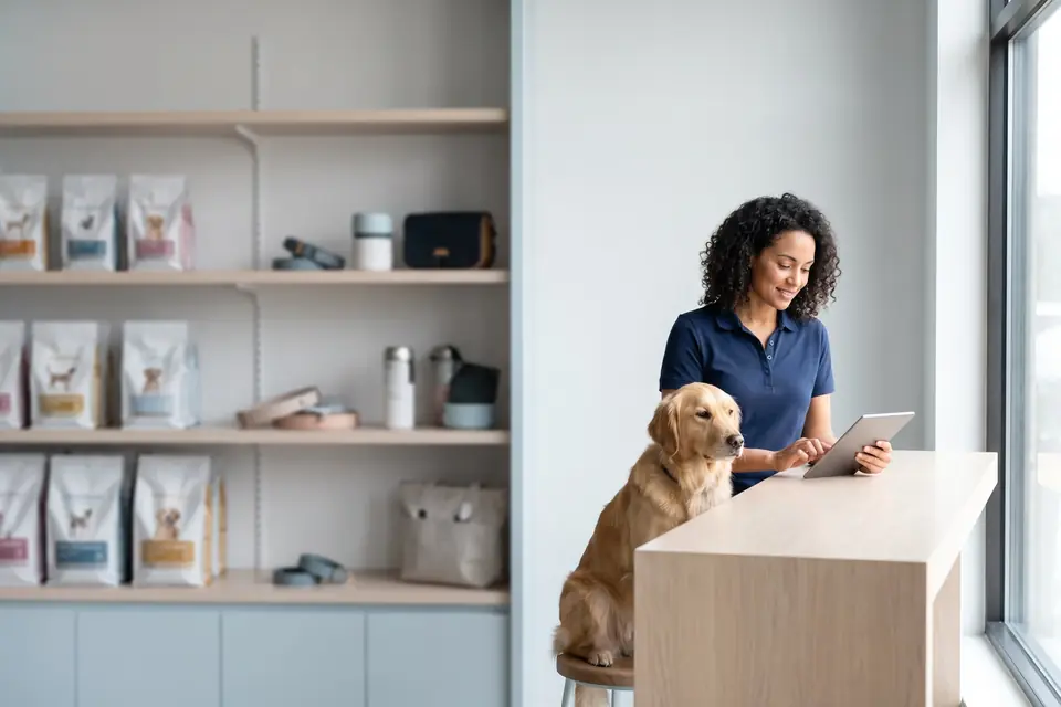 Empresária de pet shop analisando números em um tablet, com um golden retriever ao lado